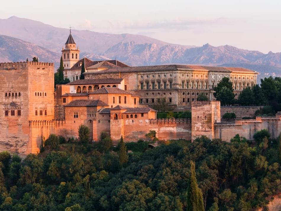 A castle-like compound surrounded by trees with mountains in the background.