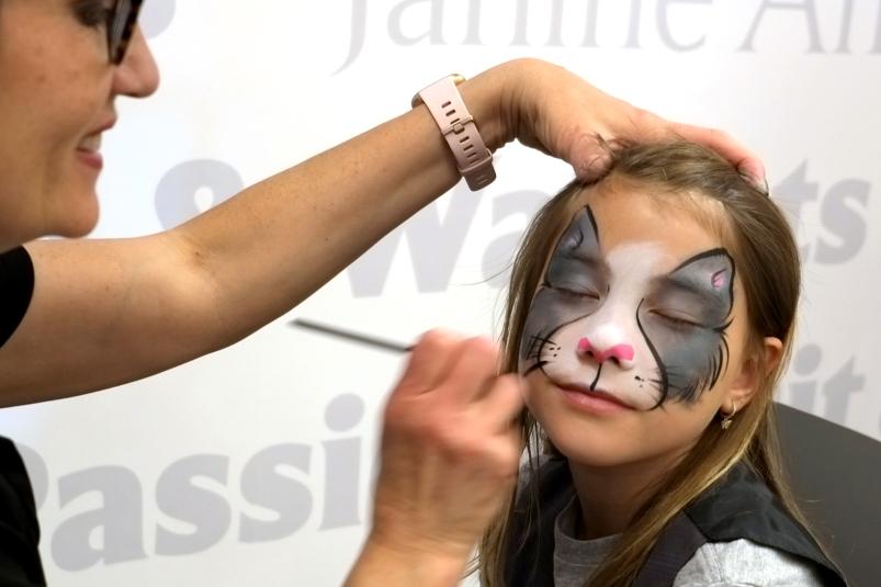 A kid having her face painted by a professional face painter.
